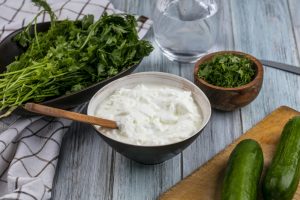 front view cucumbers on a board with yogurt and greens on a gray background