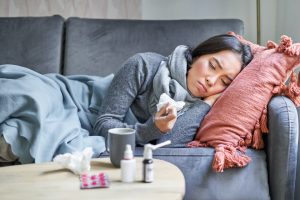 Sick sad korean woman lying on sofa, feeling unwell, catching cold, flu and temperature, looking upset, taking medication